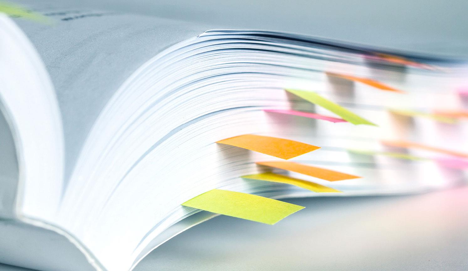 close up of the end of an opened reference book with multi coloured sticky bookmarks